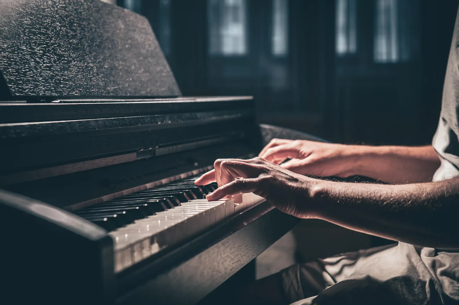 Mains posées sur le clavier d’un piano, dans la pénombre